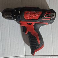 Side view of Milwaukee hammer drill driver showing the Milwaukee logo panel, torque settings on chuck, and red and black rubber grip.