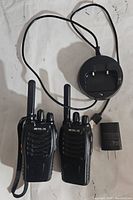 Pair of Retevis RETC 15 two-way radios shown with charging dock and power adapter on white surface.