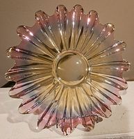 Top view photo of the iridescent glass plate showing scalloped, petal-shaped edges and a circular center base, with visible iridescence reflecting pink and gold hues.