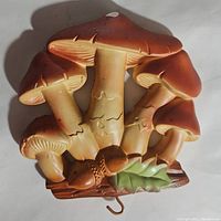Front view of mushroom chalkware wall plaque showing five mushrooms with brown caps, green leaf, and acorns on a brown base.