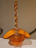 Top-down view showing the twisted clear glass handle with small decorative details and the orange glass basket body with black stripes.