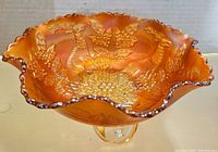 Side view of the iridescent orange carnival glass bowl with ruffled edges and raised deer and floral embossing.