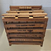 Front view of wooden slatted egg crate with 'Twin Brook Farms Garland, Maine Three Dozen Fresh Eggs' printed on side and wooden handle on top.