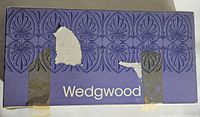 Outer Wedgwood box with purple decorative pattern and white Wedgwood logo, some tape and sticker residue visible.