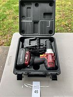 Battery powered drill with battery, charger, and case arranged in black plastic carrying case on outdoor table