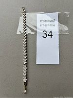 Full view of the silver tone bracelet with clear rhinestones laid flat beside a lot tag