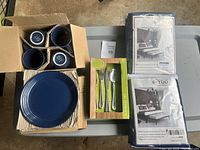 Overview of boxed blue dishware, flatware set in box, and two packaged white bedding sets on table.
