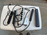 Five electrical outlet strips of various lengths and colors arranged on a white surface, including black and white strips with power cords and plug ends visible.