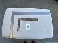 Two metal framing squares laid on a white folding table, one larger (24 inch) and one smaller (12 inch), both showing rust and wear.