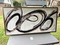 Full view of the large framed abstract painting showing swirling ovals and circular shapes in black, white, gray, with gold accents.
