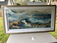 Photo of the entire large framed artwork showing abstract tidal wave design with blue, gold, and white colors.