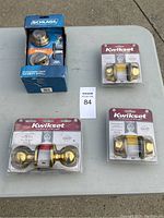 Three lock sets visible on table: Schlage deadbolt in box and two Kwikset keyed entry knob sets in plastic packaging.