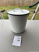 White metal ice bucket with lid, wooden side handles, black rim trim, embossed with 'ICE' on the exterior.