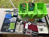 Photo showing garden tools, plastic scoops, gloves, organizer, markers, decorative glass blocks, and clothing items on table outdoors.