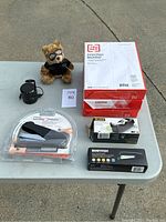 Overview of the lot showing all items on a table including paper, staplers, tape dispenser, Bluetooth speaker, and plush bear