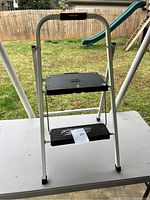 Front view of Rubbermaid two-step small step stool showing metal frame and black textured steps with the product label visible.