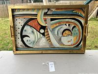 Front view of the large rectangular tray with abstract colorful artwork inside a gold frame with handles on sides.