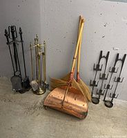 Photo of two sets of fireplace tool sets on matching stands, two copper dustpans and two small straw brooms leaning against the wall.