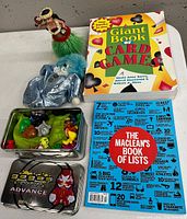 Photo of GoGo Crazy Bones tin with assorted figurines, blue plush clown doll, hula dancer figurine, and two books visible.