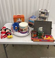 Full lot arranged on table with all items visible: Mickey and Minnie Mouse plush and puppet, Lite-Brite board, View-Master packaging, Cornflakes plate, stress doll box, coffee cans, blue troll doll