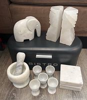Full view of marble elephant figurine, onyx bookends, marble mortar and pestle, six egg cups, and coasters arranged on top of metal storage tin