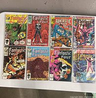 Top-down photo showing all 8 Fantastic Four Marvel comic books laid out in two rows, each comic in plastic sleeves.