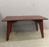 Full view of mid century modern style wood coffee table showing rectangular top and four angled legs against a gray concrete backdrop.