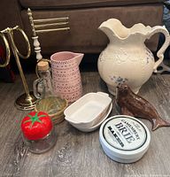 Overview of various kitchen and decorative items including pitchers, baking dishes, small figurines, and kitchen holders photographed on a wood floor.