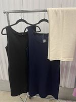 Two sleeveless knit dresses, black and navy blue, and cream knit pants hanging on a clothing rack.