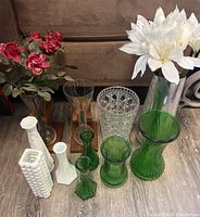 Photo showing multiple glass vases in green, clear, and milk glass with faux red and white flowers.