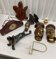 Wide view of lot contents on white table showing various vintage decor items including clocks, bookends, figurine, vase and napkin holder