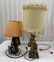 Two sets of vintage lamps; one with black and gold bases and small brown fabric shades, the other with brass floral bases and cream ruffled fabric shades.