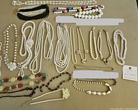 Overview of approximately 16 assorted beaded necklaces in various styles and lengths including many faux pearl strands, black, white and multicolored beads.