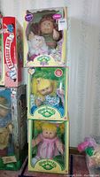 Three boxed dolls stacked vertically against wall