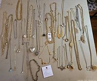 Full assortment of approximately 26 chain style necklaces laid out on table showing a variety of metals, chain styles, and pendants.