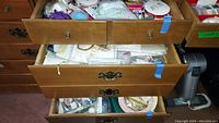 Open wooden drawers and box filled with various crafting supplies including ribbons, glue gun, and small crafting tools and materials.