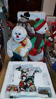 Two Gemmy animated snowmen plush figures side by side with Danbury Mint tree figurine set in styrofoam packaging in front
