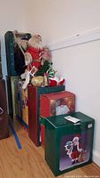 Side view of multiple boxed Santa figures stacked against a wall with visible tags and packaging.