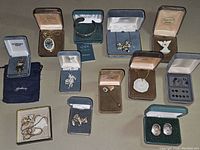 Full overview of lot showing various boxed jewelry pieces, necklaces, pins, earrings, and figurine.