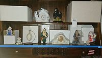 Shelf display of assorted boxed Lenox Santa figurines, mantel clocks, and ornaments wrapped in paper and boxes.