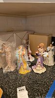 Full view of 5 Lenox porcelain figurines on a dark countertop with original boxes in background. One figurine wrapped in plastic.