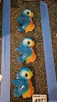 Three vintage chalkware blue birds arranged in a line on a textured surface with blue painter tape on either side.