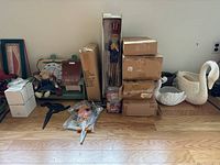 Overview of the lot items grouped on floor including boxed and loose items such as tall Uncle Sam, swan planters, dog lawn sign, stacked boxes