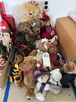 Group of assorted stuffed Boyd's Bears and similar plush bears, medium to large sizes, arranged on floor with some wearing floral and fabric accessories.