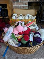 Wide view of basket with assorted yarn skeins, with floral cardboard box containing more yarn in background.