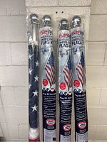 Four flag kits vertically displayed against a wall showing flags wrapped and kits packaged with labels indicating US flag and Betsy Ross brand.