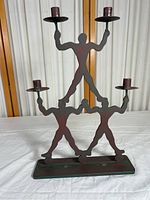 Full view of the cast iron gymnast candle holder showing three stylized gymnast figures stacked, each holding a candle cup. The holder has a dark metal finish and stands on a rectangular base.