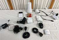Overview of lot items including white keypad, base station with tower speaker, white motion and entry sensors, various power adapters, and cables on white surface.