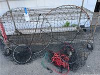Two cylindrical crab fishing nets displayed outdoors on a metal cart, showing overall condition and size