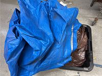 Blue tarp with silver reflective stripes partially unfolded on floor next to container